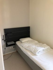 Sovrum med säng, lampa och sängbord. 