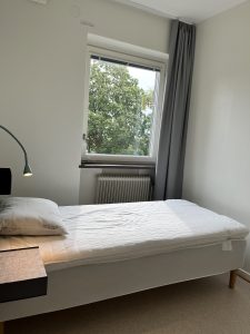 Sovrum med säng, sängbord och fönster.