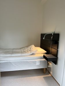 Sovrum med säng, lampa och sängbord.