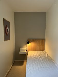 Sovrum med säng, sängbord och lampa.
