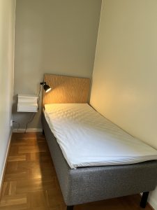 Sovrum med säng, lampa och sängbord.