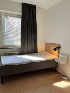 Sovrum med säng, lampa och sängbord.