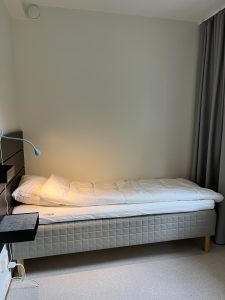 Sovrum med säng, lampa och sängbord.